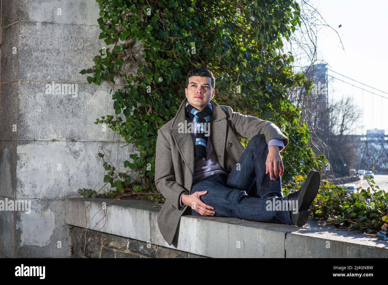 Ein junger Mann, der auf einem großen Rahmen sitzt und vor wilden grünen Pflanzen sitzt, schaut nach oben und denkt tief nach. Stockfoto