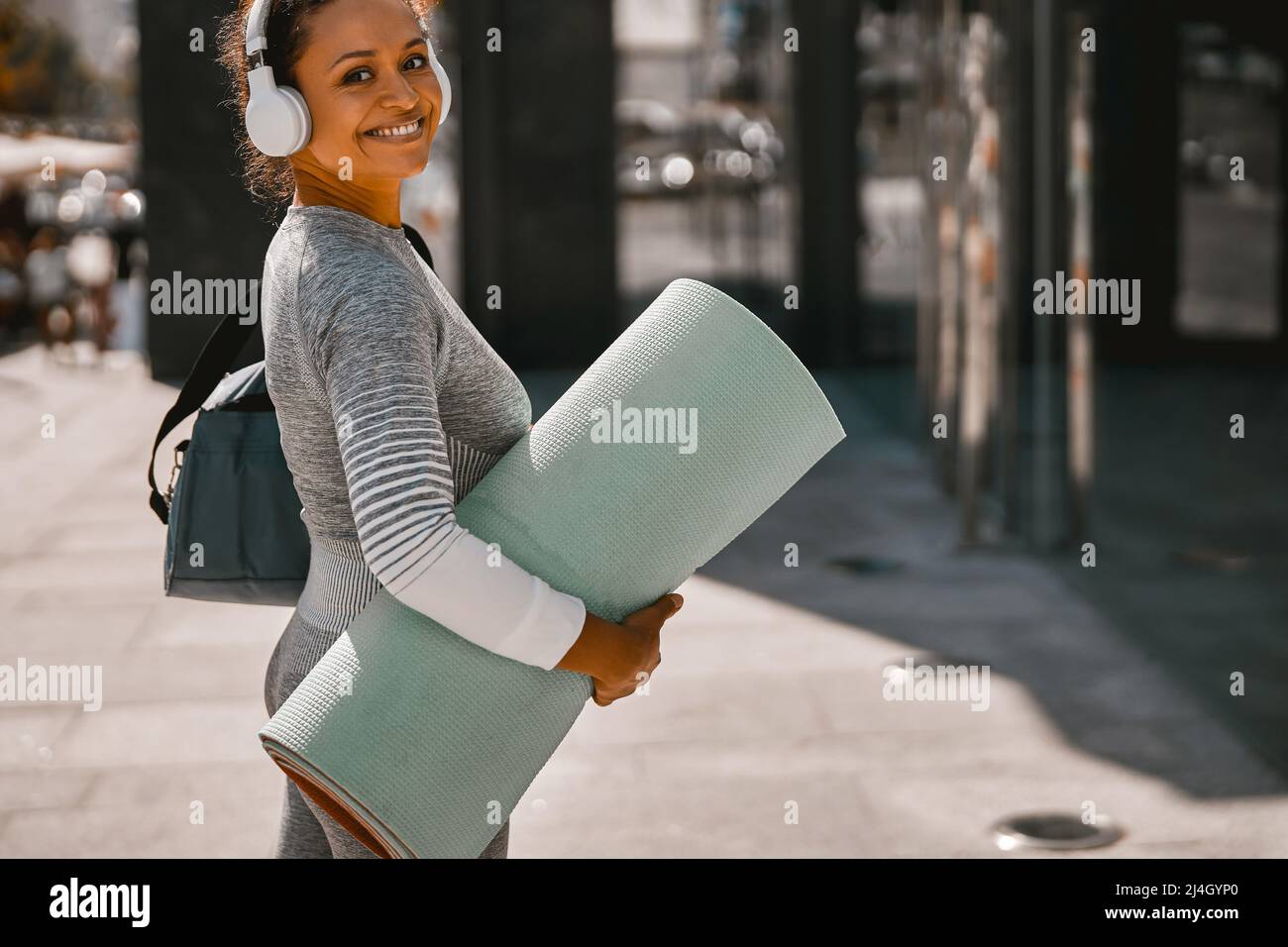 Fröhliche Frau in Sportkleidung lächelt vor der Kamera, während sie in der Stadt trainieren geht Stockfoto