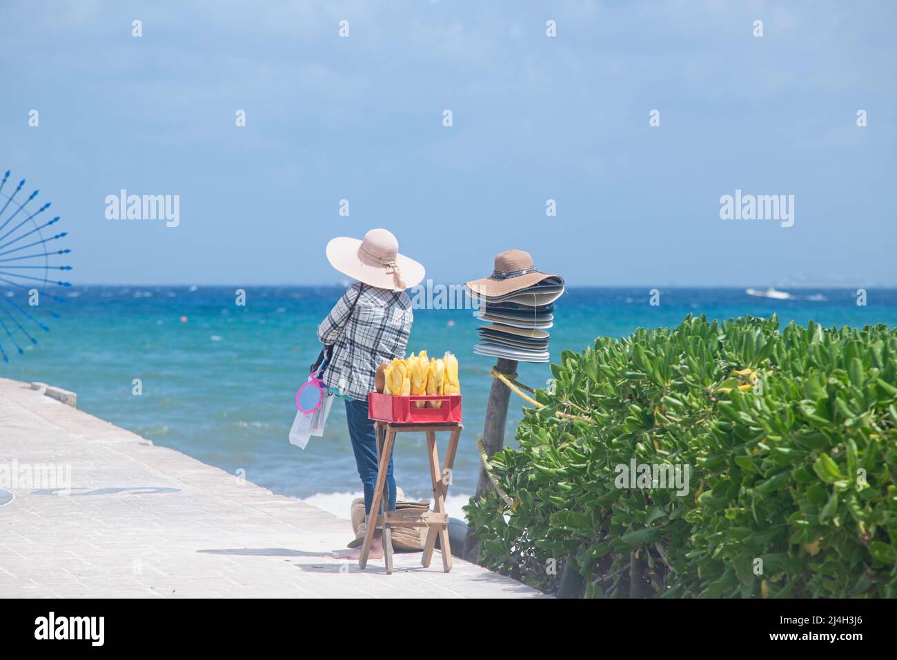 Eine mexikanische Frau, die in der Nähe des Strandes in Playa del Carmen, Mexiko, tropische Früchte und Hüte verkauft Stockfoto