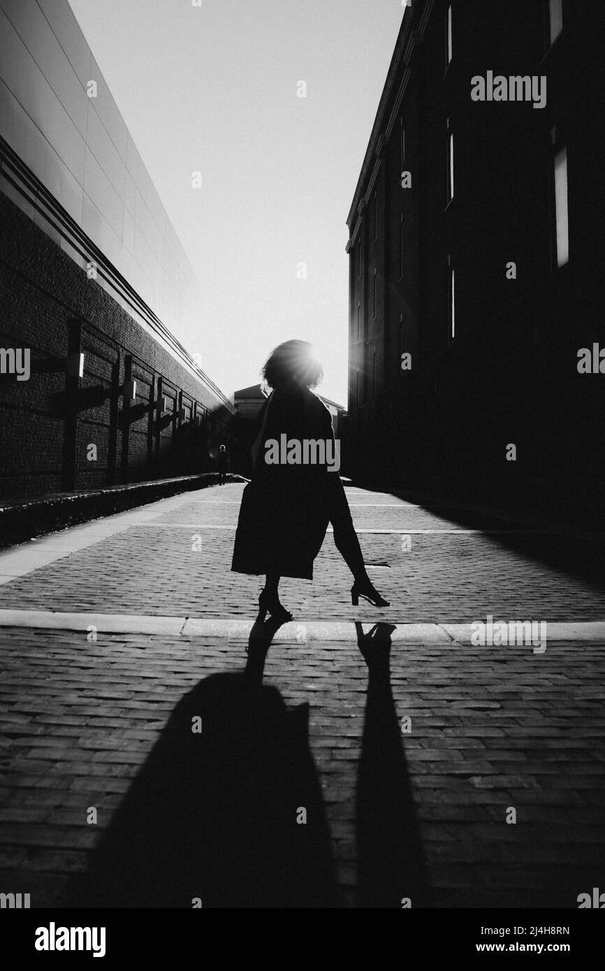 Schwarze Frau, die stark steht und die Abschlusskappe in die Luft wirft. Silhouette Foto zwischen zwei Gebäuden. Stockfoto