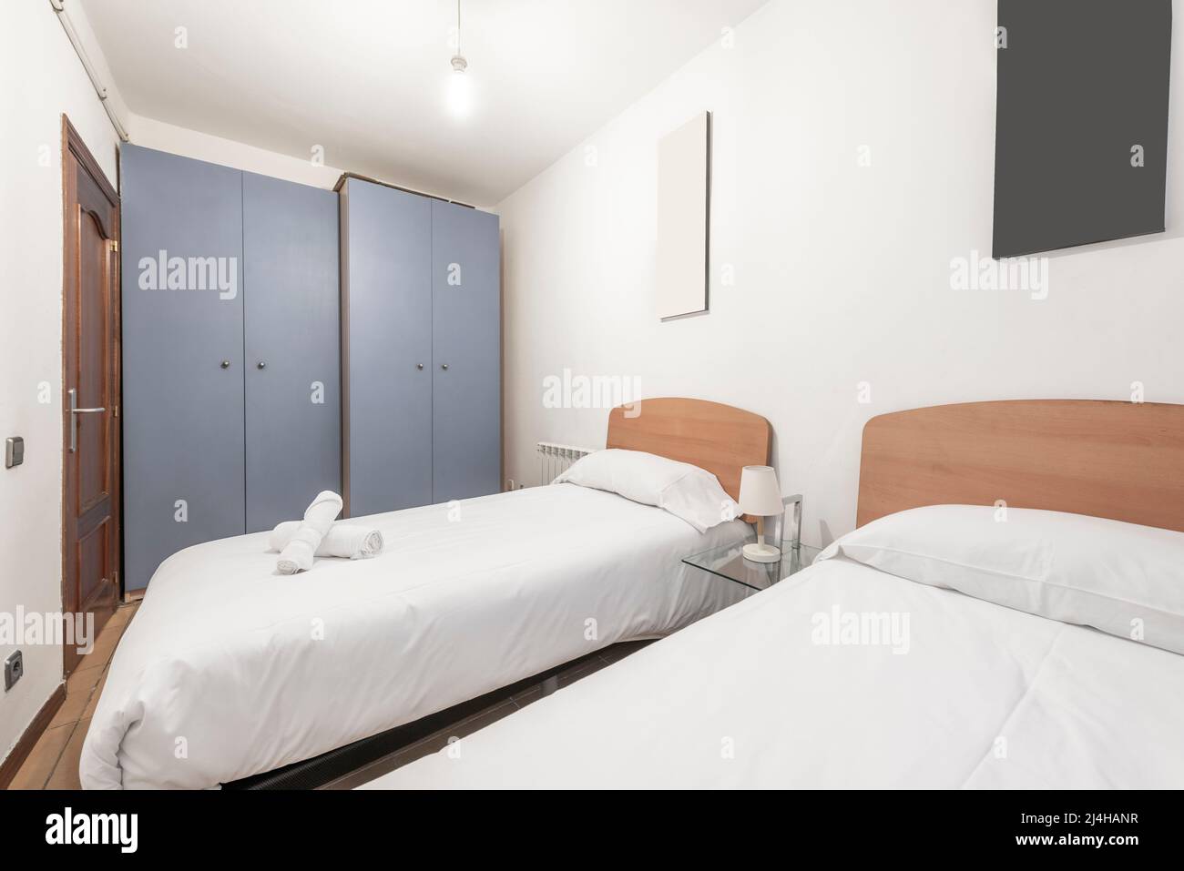 Schlafzimmer mit Twin-Betten mit Kopfteilen aus hellem Holz mit weißen Bettdecken und zwei grauen Schränken Stockfoto