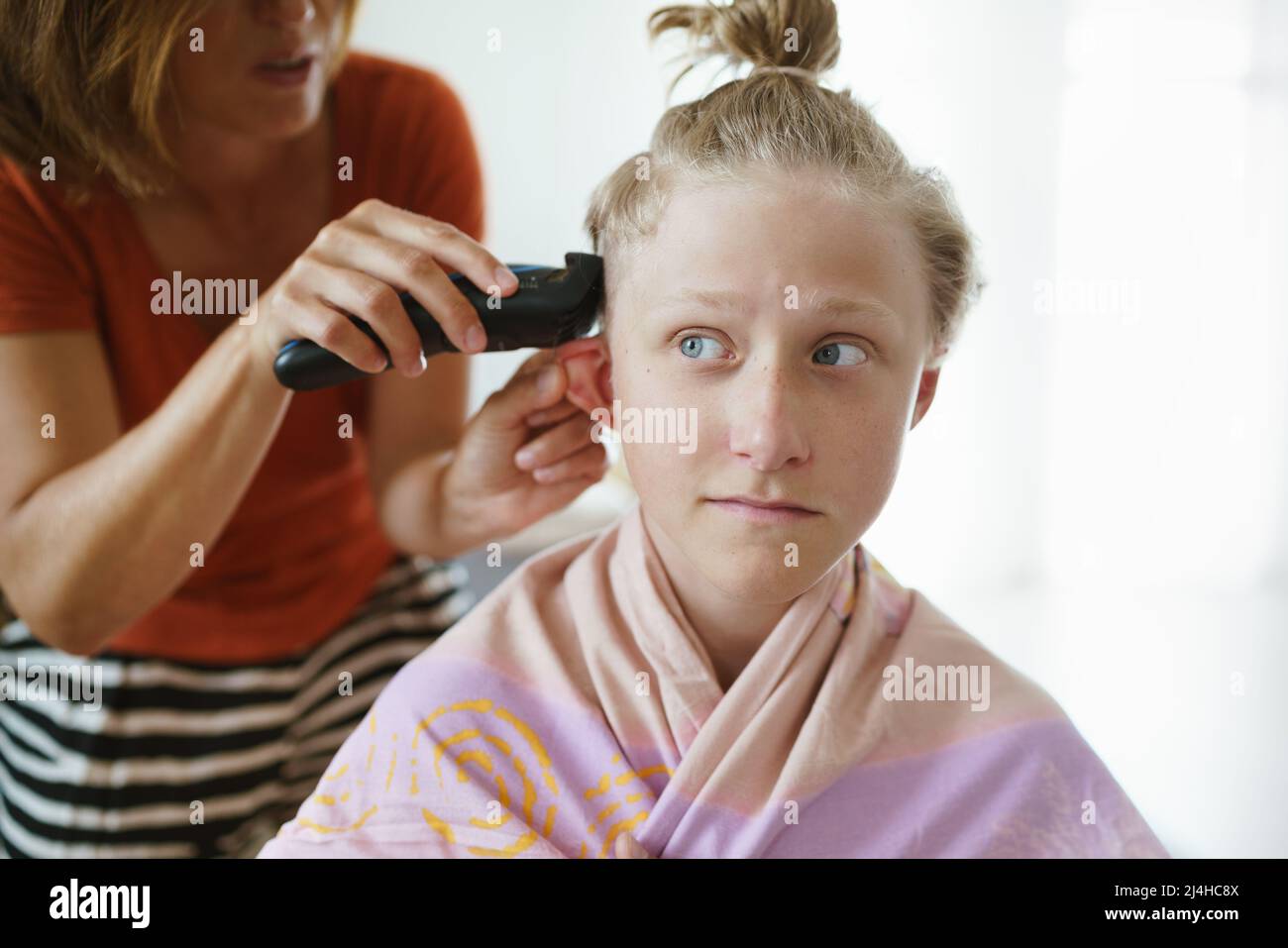 Mutter schneidet Haare ihres Sohnes und macht eine moderne Frisur mit einem elektrischen Trimmer im Wohnzimmer. Stockfoto