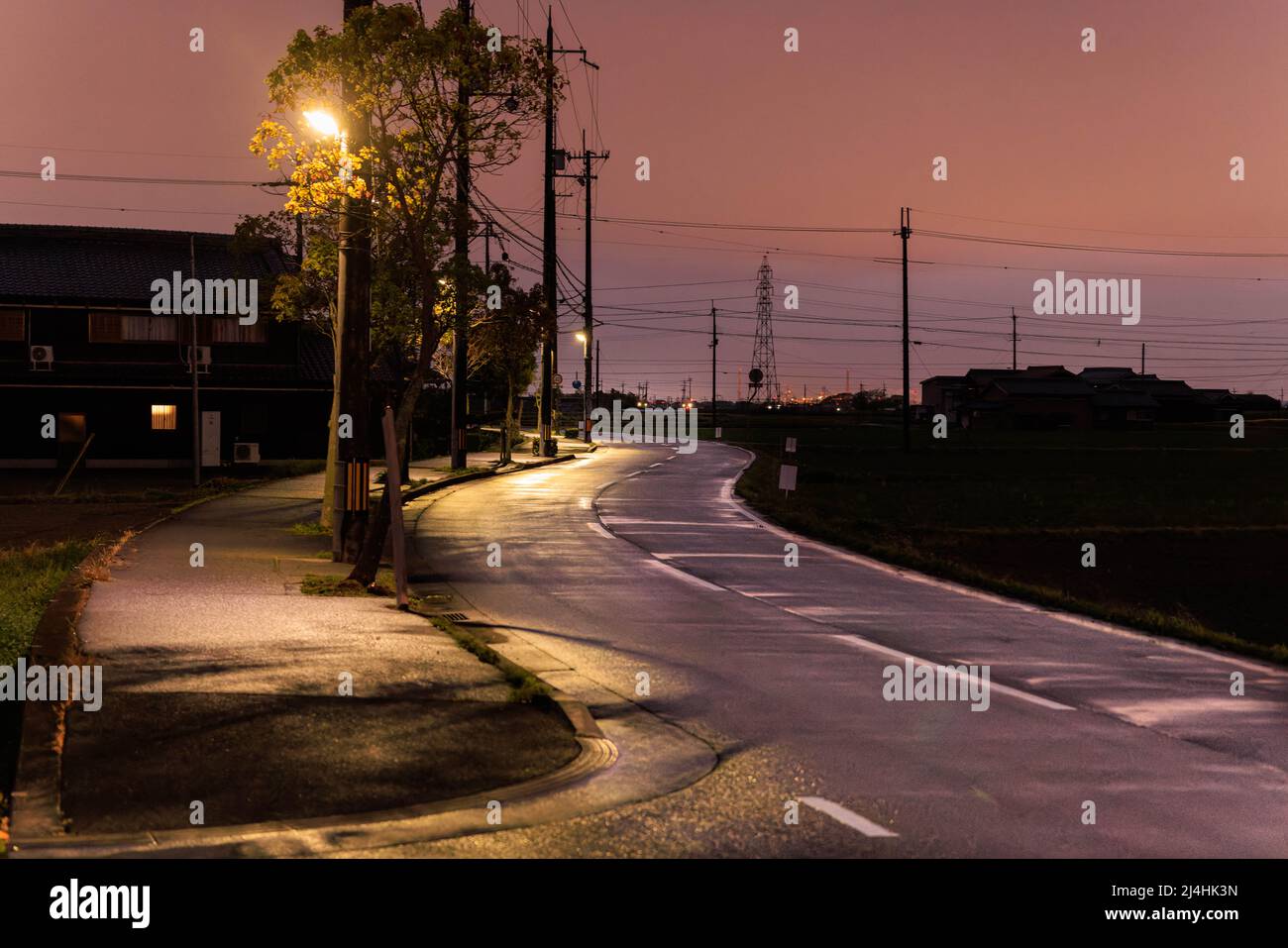 Rötlich glühend über nasser, gewundener Straße durch ländliches Land bei Sonnenuntergang Stockfoto