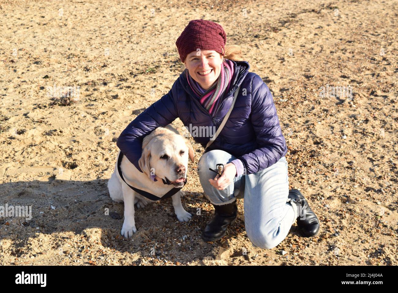 Lächelnde Frau mit Hund am sonnenbeschienenen Strand. Stockfoto