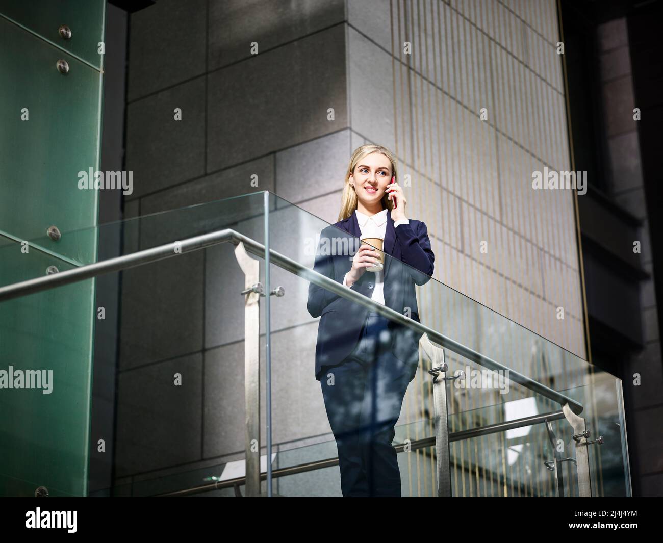 Junge kaukasische Geschäftsfrau, die auf einer Treppe steht und mit dem Mobiltelefon in einem modernen Bürogebäude telefoniert Stockfoto