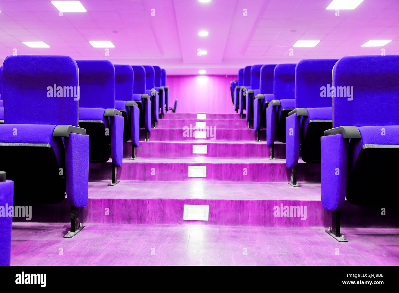 Treppenhaus Galerie zwischen leeren Reihen von Sitzen eines Auditoriums mit violett liegenden Reihen von Sitzen und abgehängte Decke führte Lichter. Stockfoto