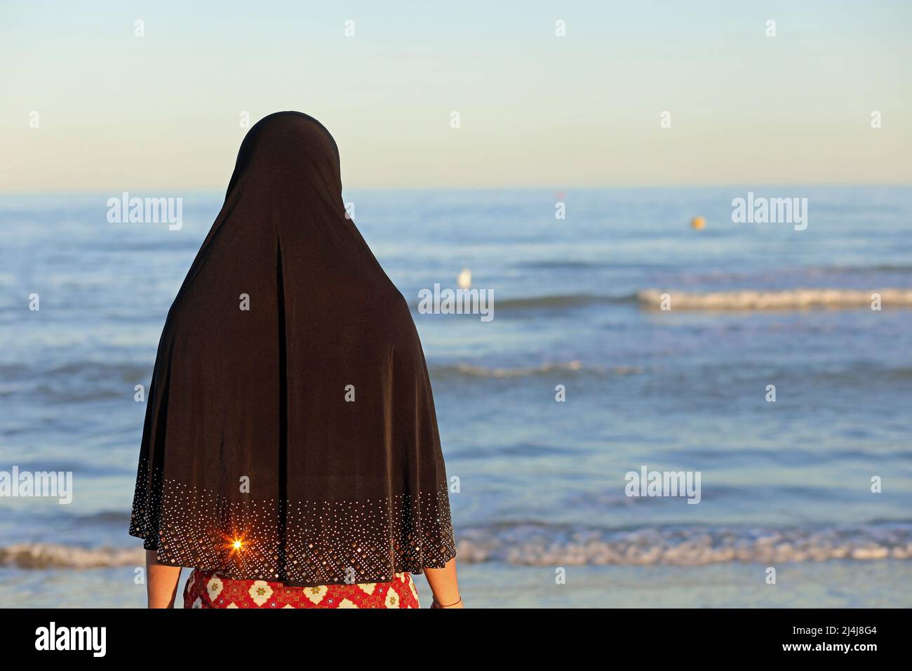 Junge Frau mit langem schwarzen arabischen Schleier wartet auf Ankünfte am Meer Stockfoto