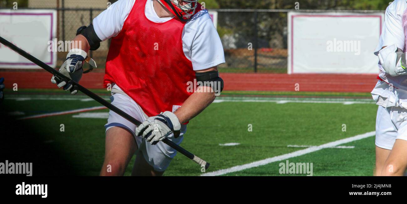 Eine Nahaufnahme eines High School Boy Lacrosse Spielers, der mit dem Ball während einer Scrimmage auf den Angriff läuft. Stockfoto