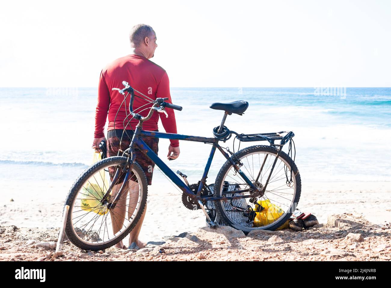 Ein Mann, der am Strand neben seinem Fahrrad steht, mit dem Strand von Boca do Rio im Hintergrund. Salvador, Bahia, Stockfoto