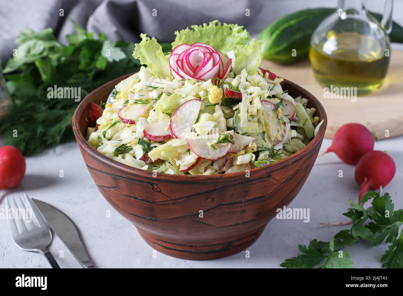 Salat mit Kohl, Gurken, Radieschen, Petersilie und Ei, gewürzt mit Olivenöl in einer braunen Schüssel auf grauem Grund Stockfoto