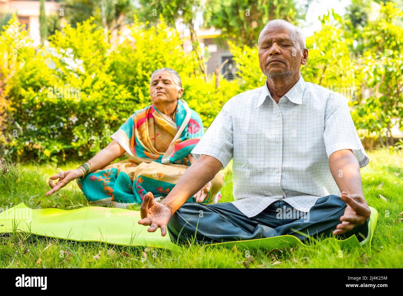 Seniorenpaar auf Yogamatte meditiert morgens im Park mit geschlossenen Augen - ein Konzept der Entspannung, eines gesunden Lebensstils und der Selbstversorgung Stockfoto