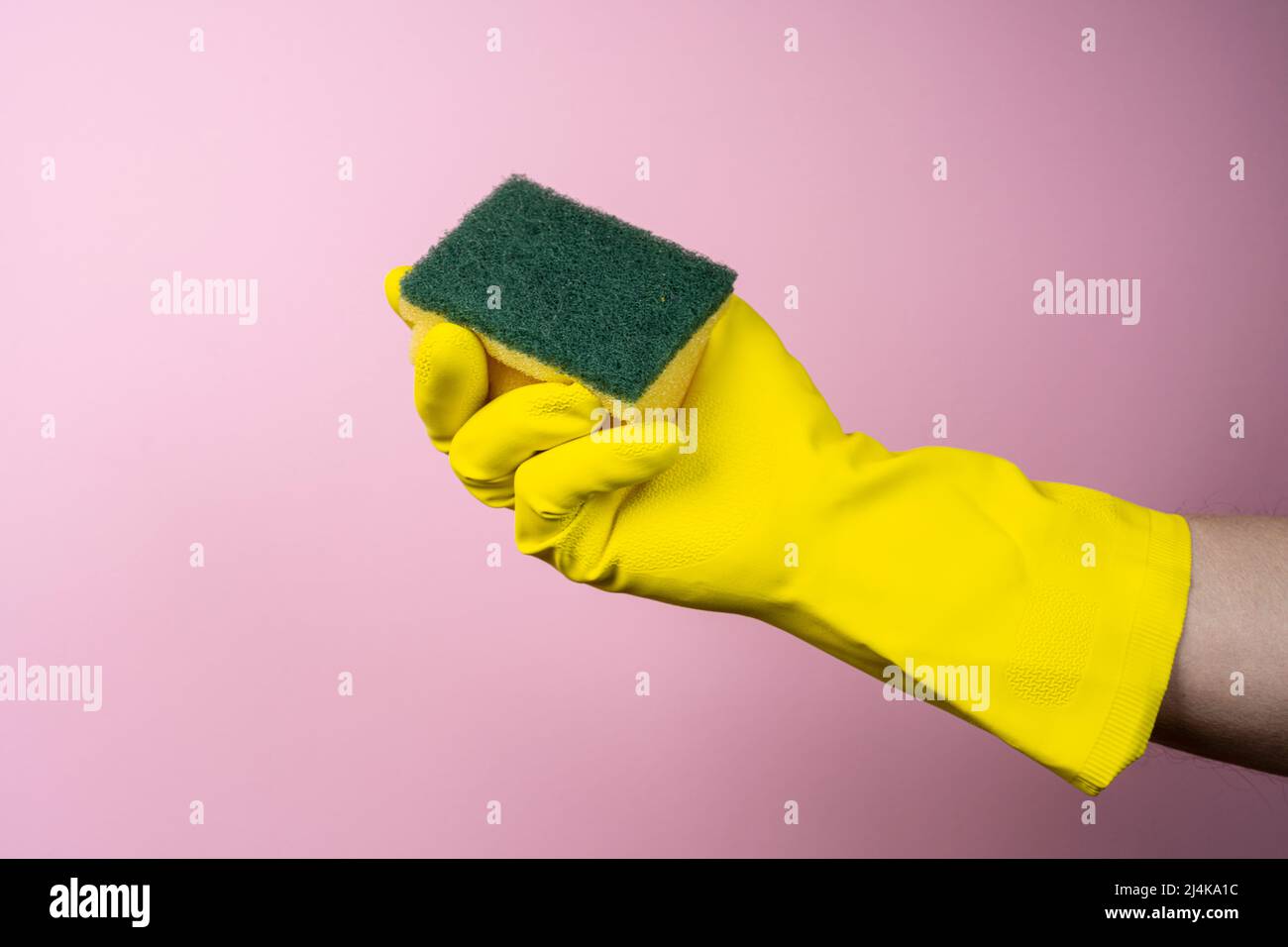 Eine Hand mit einem gelben Gummihandschuh hält einen Reinigungsschwamm Stockfoto