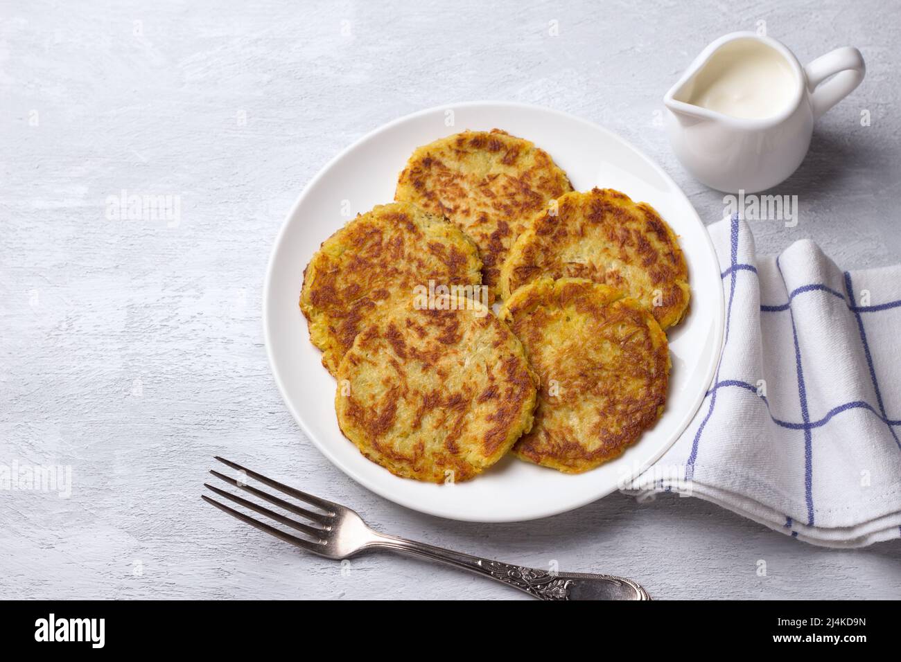 Traditionelle Latkes Krapfen mit saurer Creme auf einem hellgrauen strukturierten Hintergrund mit freiem Platz, Draufsicht Stockfoto