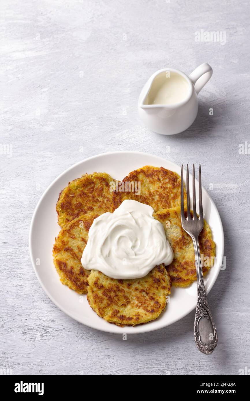 Traditionelle Latkes-Krabben mit saurer Creme auf hellgrauem texturiertem Hintergrund, Draufsicht Stockfoto