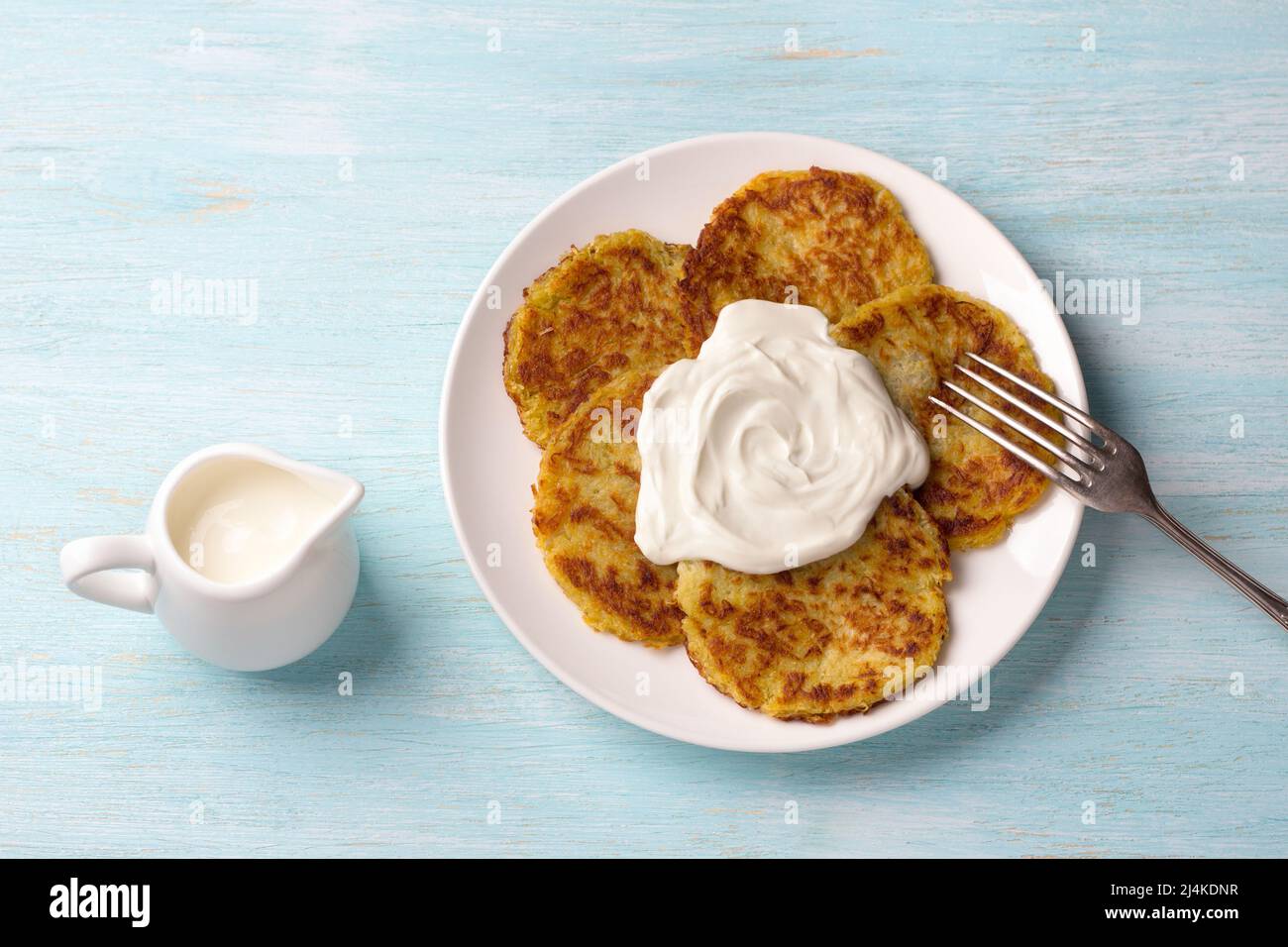 Traditionelle Latkes-Krabben mit saurer Creme auf hellblauem texturiertem Hintergrund, Draufsicht Stockfoto