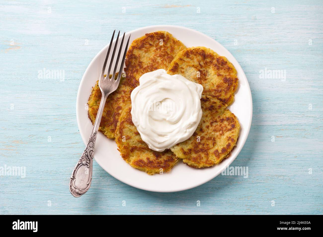Traditionelle Latkes-Krabben mit saurer Creme auf hellblauem texturiertem Hintergrund, Draufsicht Stockfoto