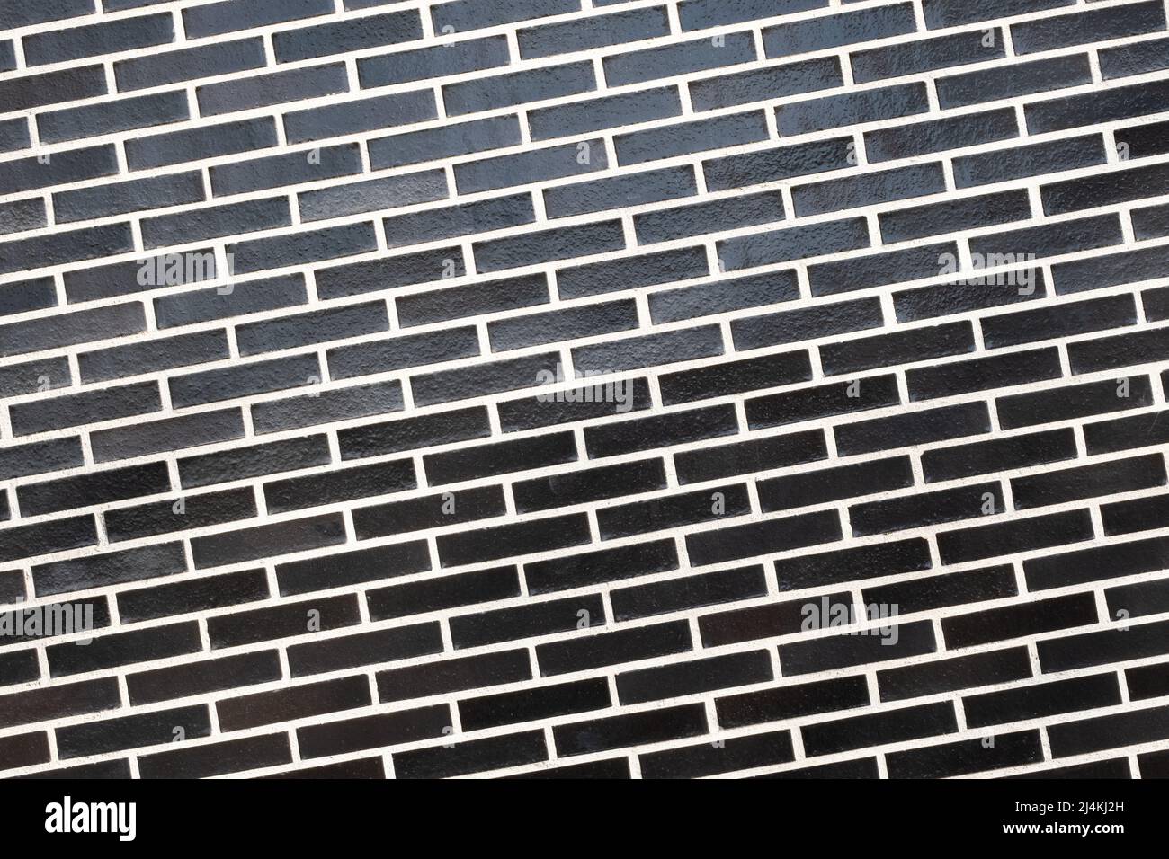 Eine schwarze Ziegelwand mit weißer Fugenlinie, schräg angeschrägte Ebene. Abstrakter Hintergrund mit Kopierbereich Stockfoto