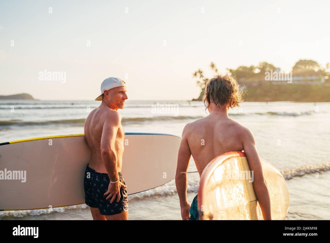 Teen boy mit Surfbrett gehen zum Meer zum Surfen mit Vater auf Sri Lanka Insel. Sie haben einen Winterurlaub und genießen ein wunderschönes Sonnenuntergangslicht Stockfoto