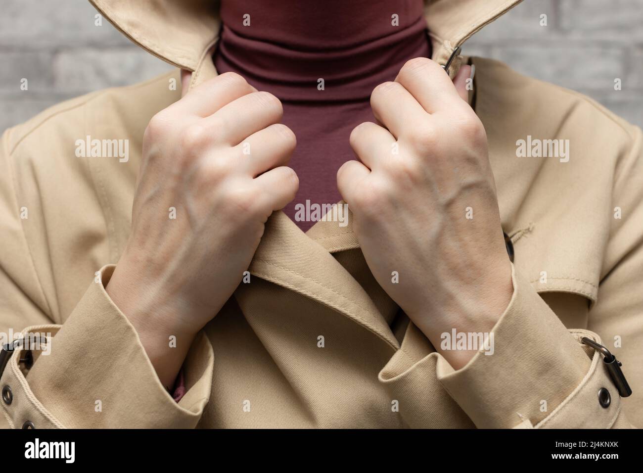 Eine Frau in einem Regenmantel legt ihre Hand auf den Revers ihres Kragens. Hochwertige Fotos Stockfoto