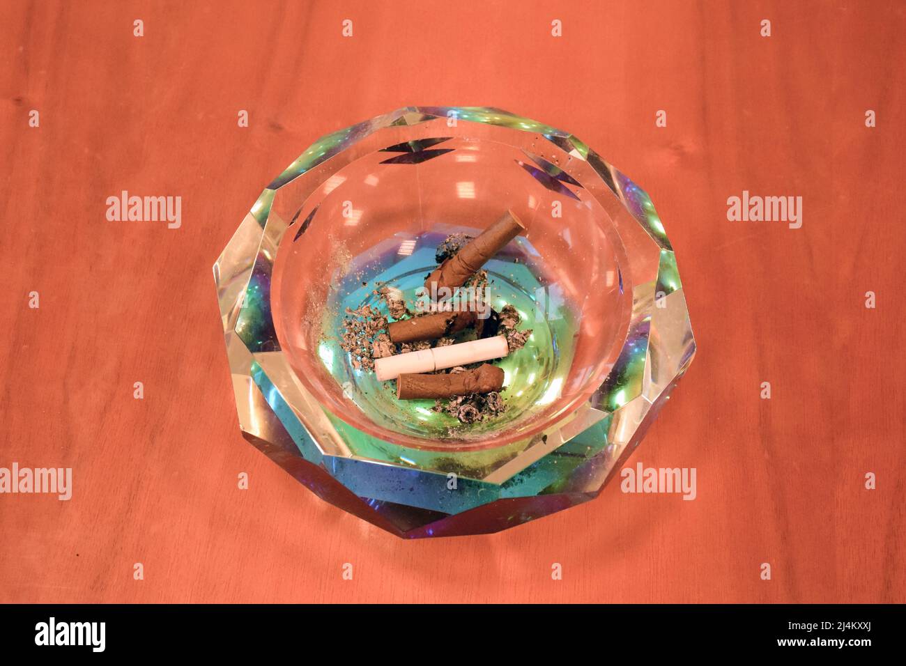 Auf der hölzernen Oberfläche des Tisches liegt ein Kristallaschenbecher mit Zigarettenkippen verschiedener Zigarren und Zigaretten. Nahaufnahme Stockfoto