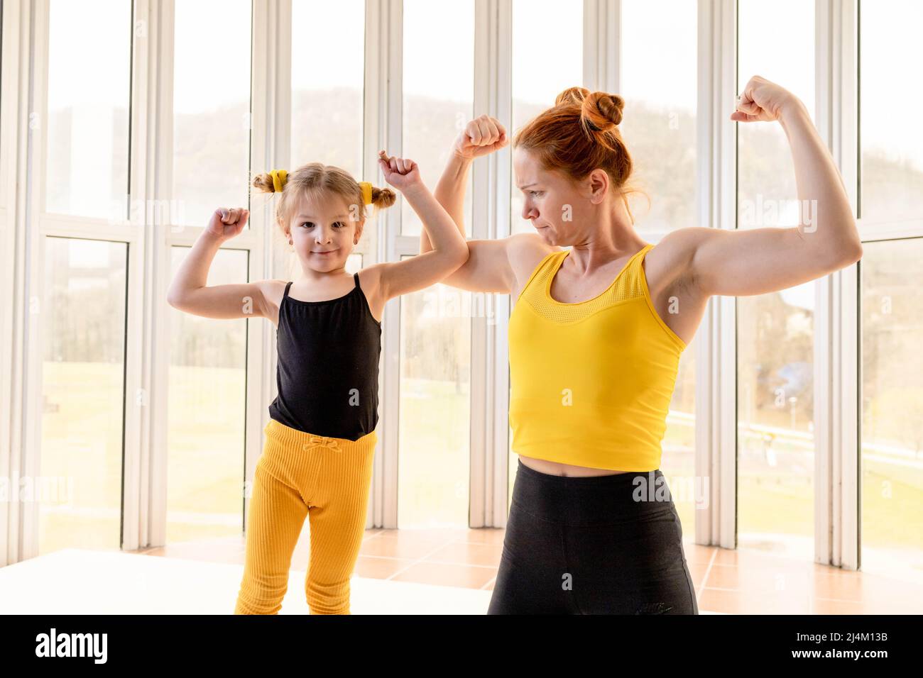 Junge fit Mutter und ihre Tochter in passenden Kleidern, zeigen Muskeln. Fitness-Motivation Stockfoto