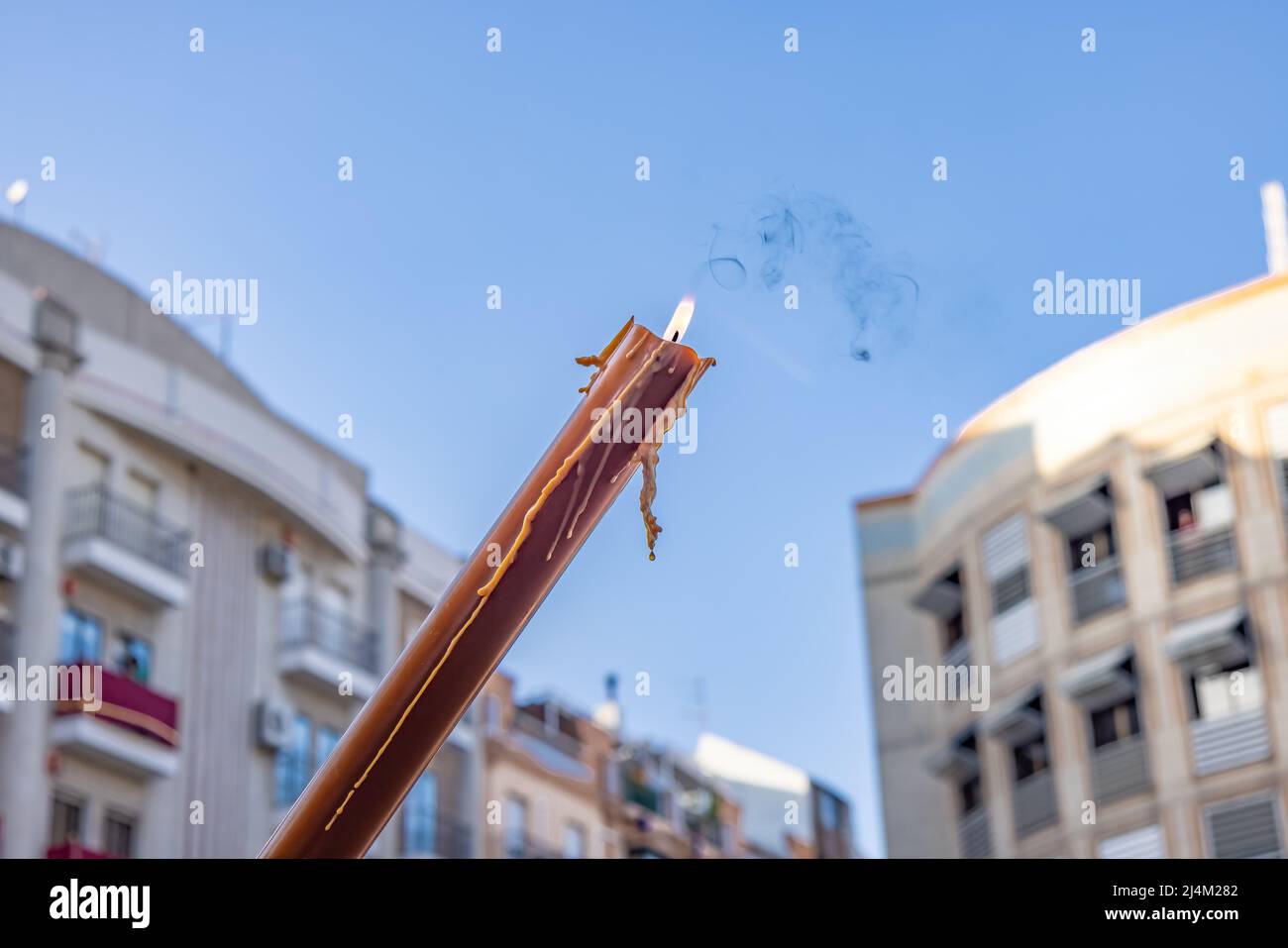 Eine braune Kerze mit der brennenden Flamme eines Nazareners oder Büßers in Prozession zur Karwoche gegen den blauen Himmel. Die Kerze wird am W der Person gehalten Stockfoto