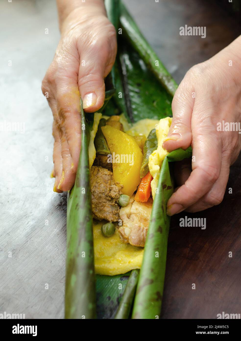 Einheimische Frau, die traditionelle kolumbianische Gerichte mit Maisteig zubereitet und mit Huhn, Schwein, Schweinerippchen und Gemüse gefüllt hat; in Bananenblätter gewickelt. Stockfoto