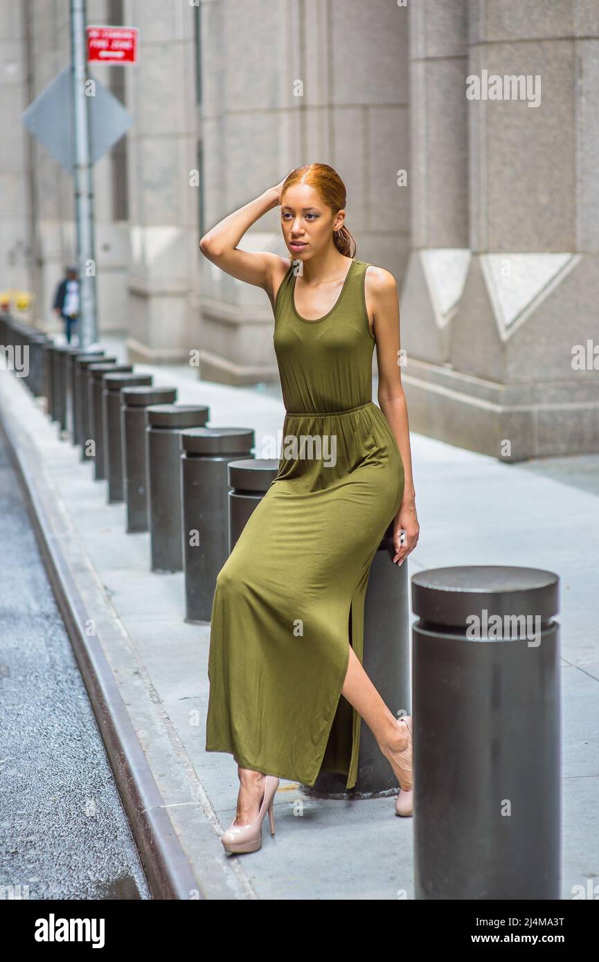 Frau, Die Sich Auf Steet Entspannt. In einem grünen Maxi Tank Dress, hohen Absätzen, einer Hand, die ihren Kopf berührt, sitzt ein junges schwarzes Mädchen auf schwarzem Metall Colu Stockfoto