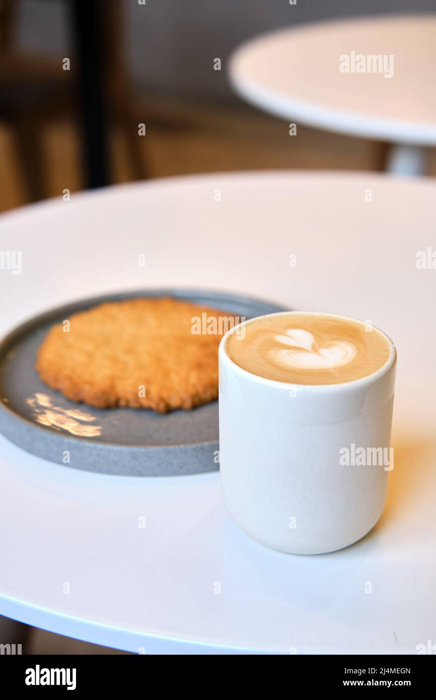 Der morgendliche Brunch im Café ist auf dem Tisch. Riesenkeks und Cappuccino mit schönem Milchschaum. Manchmal muss man in dieser schnelllebigen Welt eine Pause einlegen Stockfoto