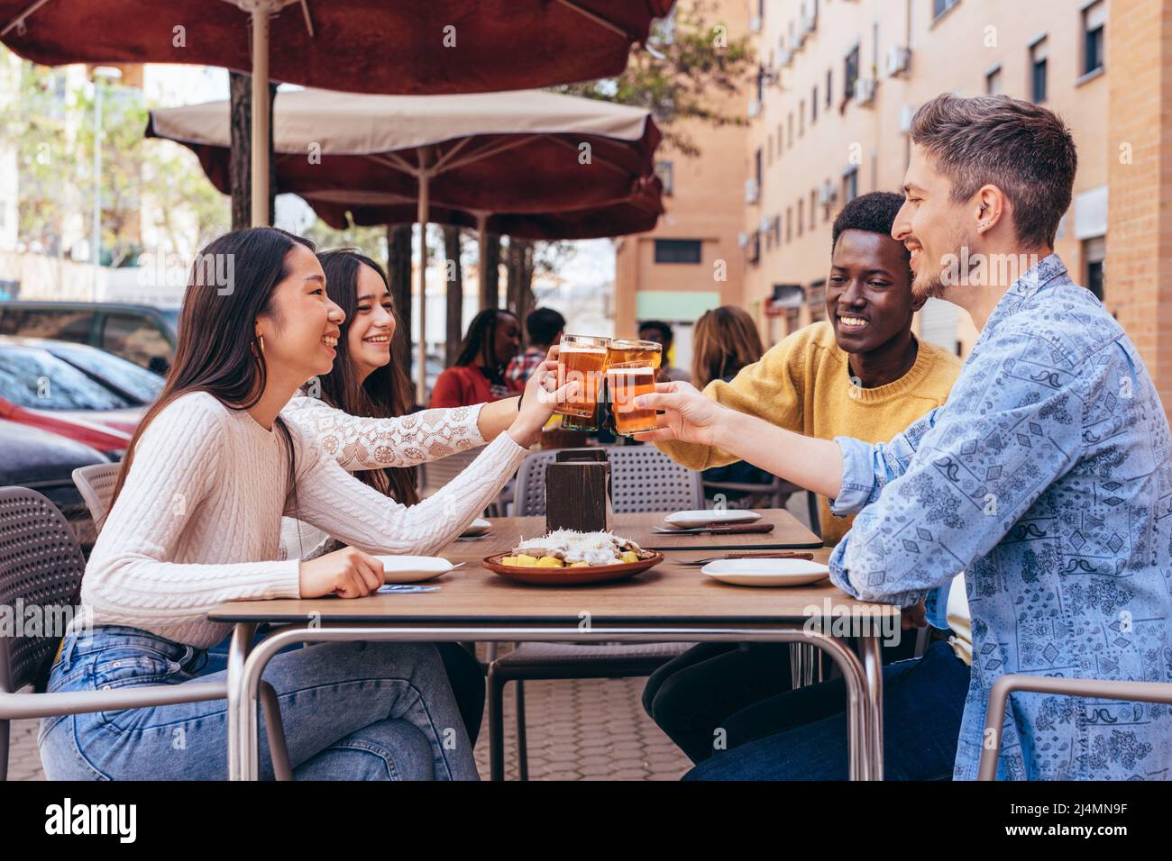 Eine multiethnische Gruppe von 4 Freunden, die auf der Restaurantterrasse toasten Stockfoto