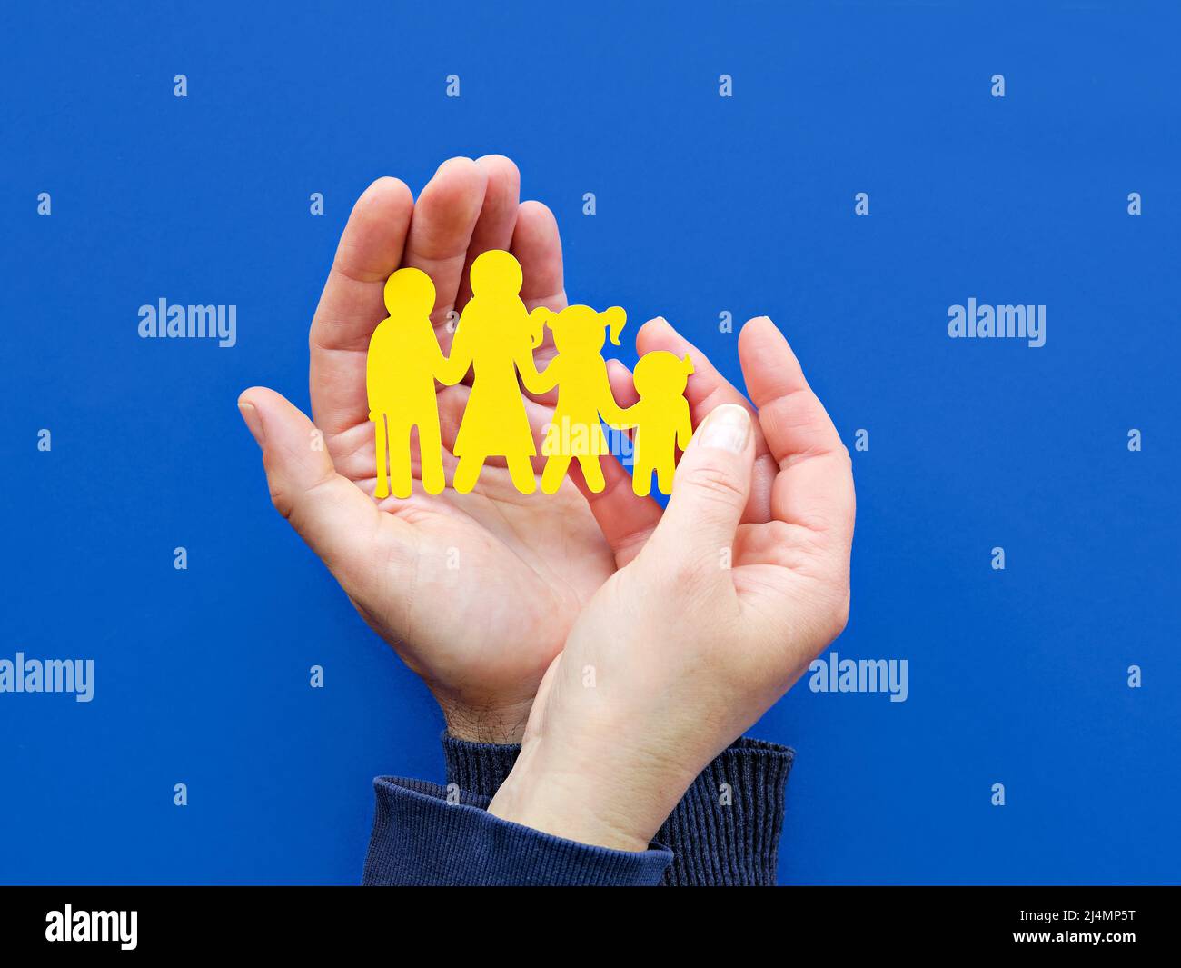 Helfende Hände, männlich und weiblich, mit gelber Papiersilhouette der ukrainischen Familie. Flach liegend, Draufsicht auf blauem Hintergrund. Stockfoto