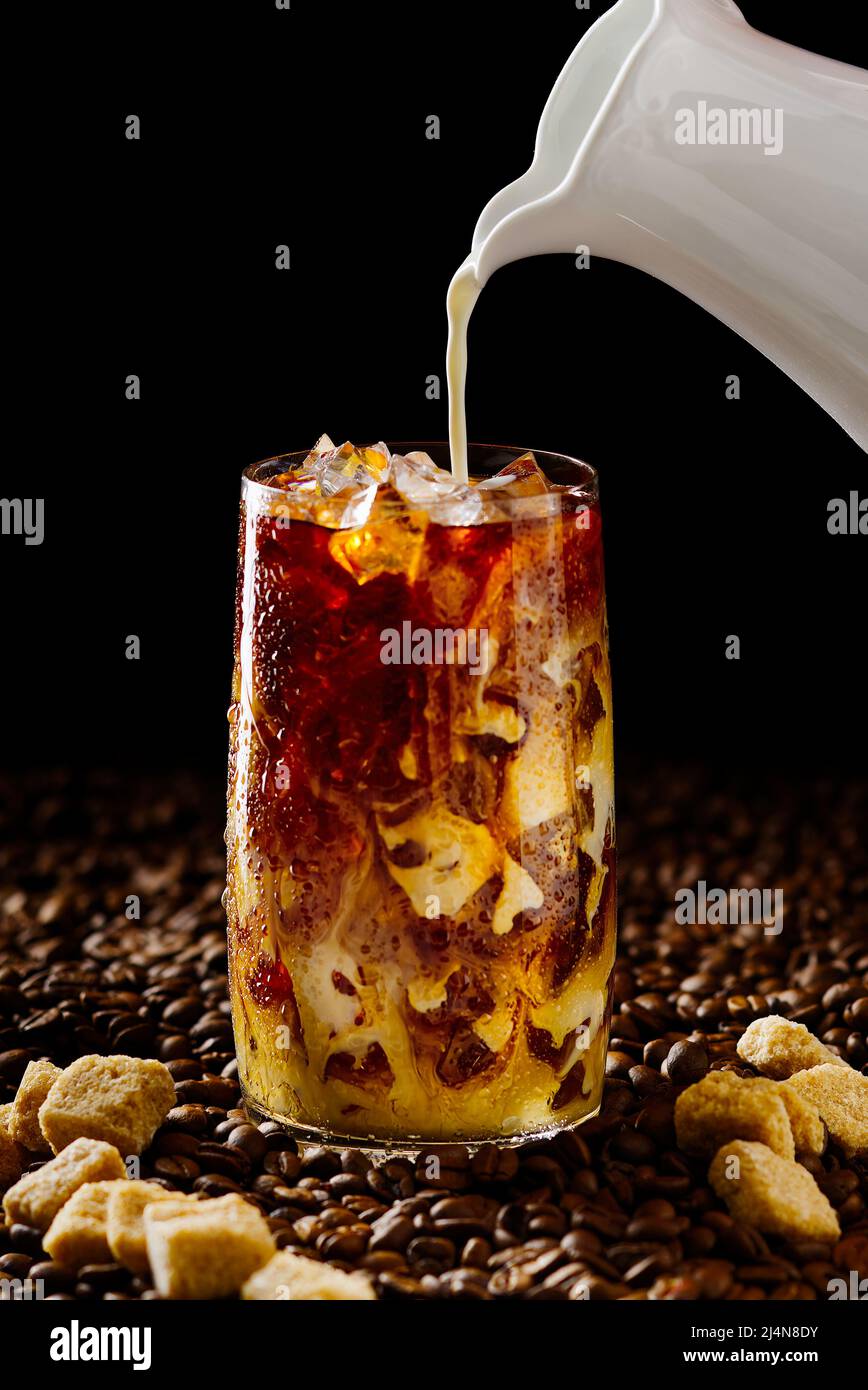 Eiskaffee. Leckerer Eiskaffee mit Milch, kaltes Getränk im Glas mit Eis auf dunklem Kaffeehintergrund. Stockfoto