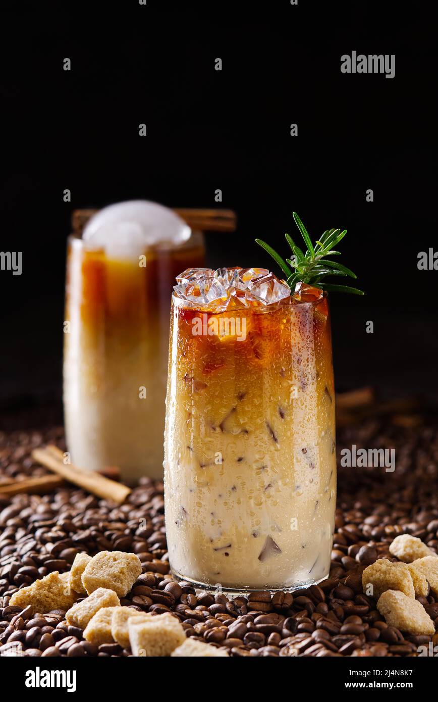 Eiskaffee. Leckerer Eiskaffee mit Milch, kaltes Getränk im Glas mit Eis auf dunklem Kaffeehintergrund. Stockfoto