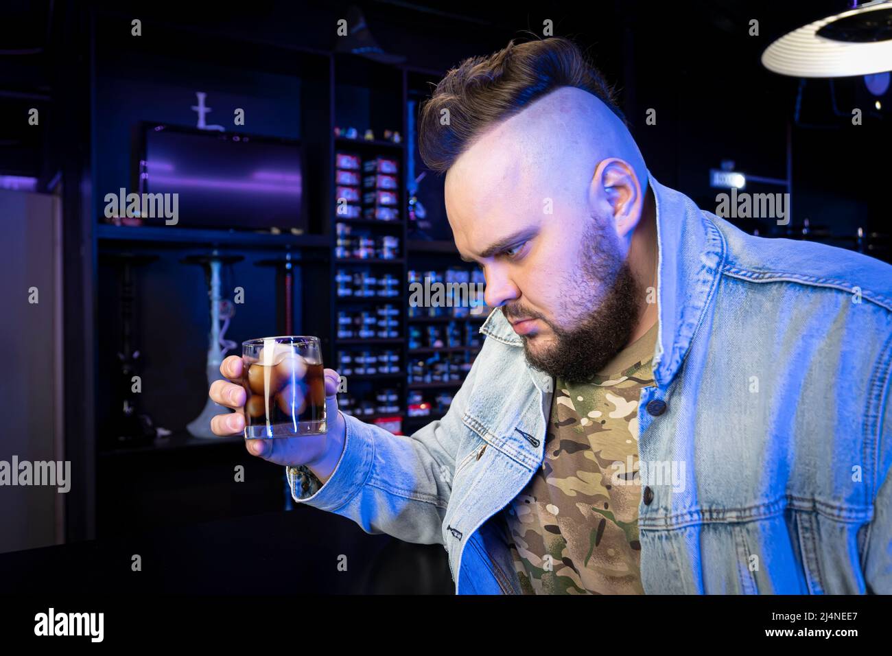 Ein betrunkener brutaler Mann mit einem alkoholischen Cocktail in einem Glas. Das Konzept der schlechten Gewohnheiten und Alkoholabhängigkeit. Einsamer trauriger Mann wird in einem irischen Pub betrunken Stockfoto