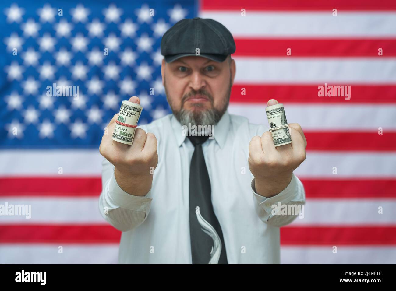 Ein Mann zeigt den Mittelfinger, auf dem Dollar in einen Schlauch gerollt werden. Geste - Sie erhalten kein Geld. Vor dem Hintergrund der US-Flagge. Stockfoto