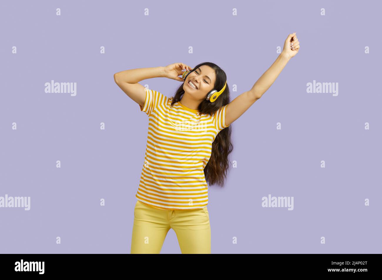 Wunderschöne Brünette junge Frau, die Musik in Kopfhörern hört, tanzt und singt mit geschlossenen Augen auf violettem Hintergrund. Stockfoto