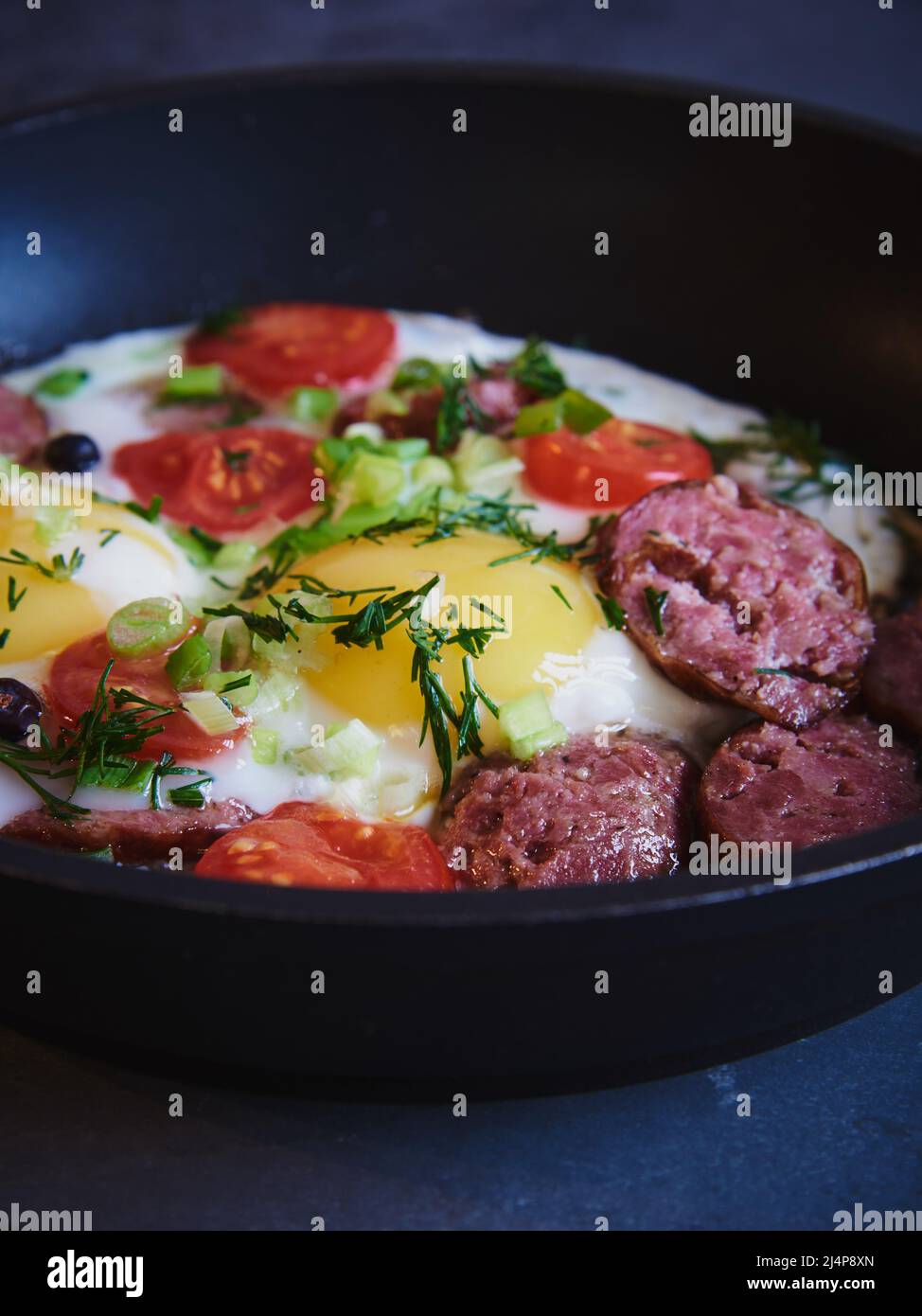 Spiegeleier mit geräucherter Wurst, Tomaten und Kräutern in einer Pfanne. Stockfoto