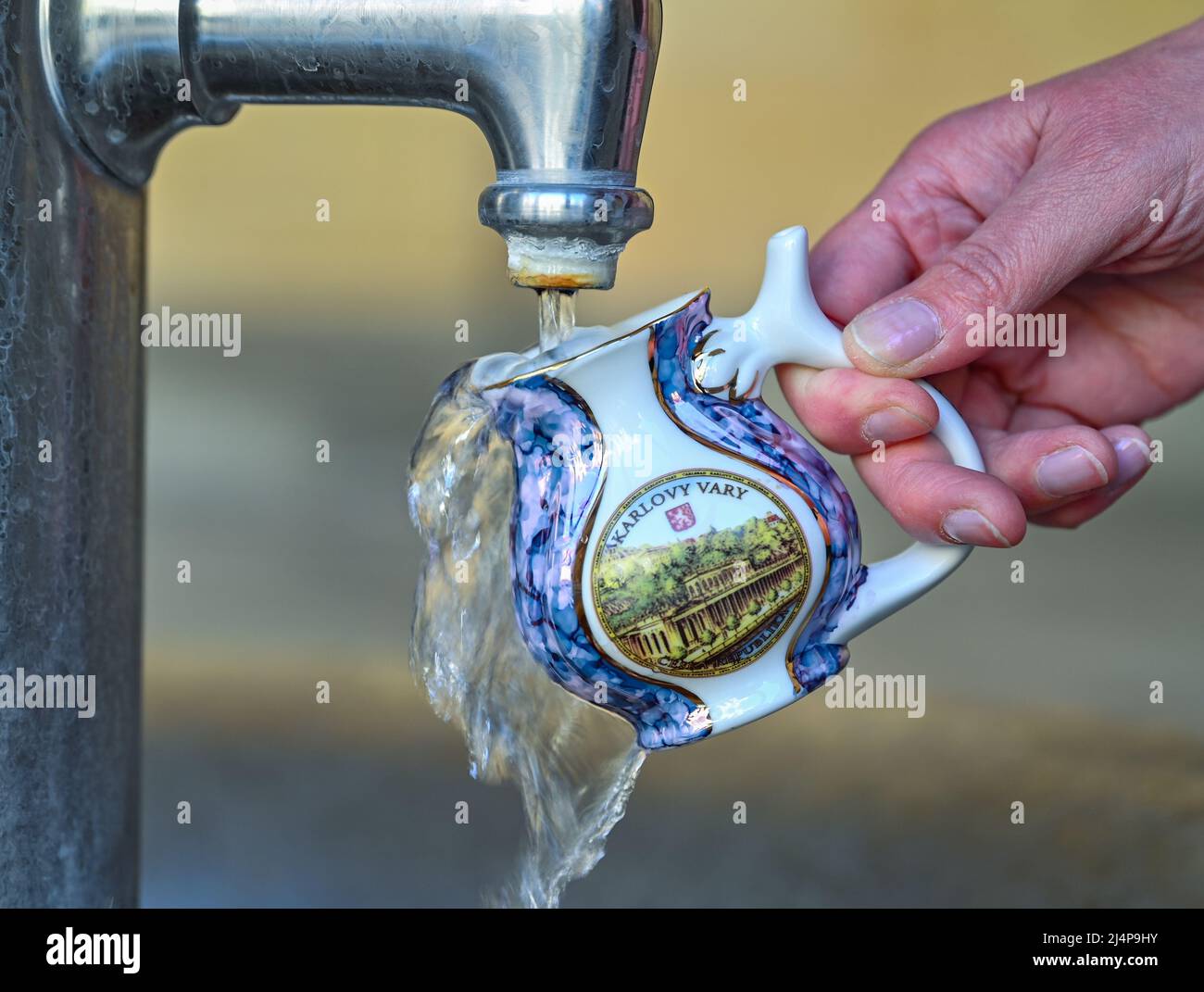 11. April 2022, Tschechische Republik, Karlovy Vary: Eine Frau holt Wasser aus einer heißen Quelle im Zentrum von Karlovy Vary (Tschechisch: Karlovy Vary) mit einem original Karlsbader Schnabelbecher. Karlovy Vary ist eine Kurstadt in der Region Böhmen im westlichen Teil der Tschechischen Republik. Dank seiner zahlreichen Thermalquellen ist die Stadt am Rande des Erzgebirges seit dem 19.. Jahrhundert ein beliebtes Touristenziel. Foto: Patrick Pleul/dpa Stockfoto