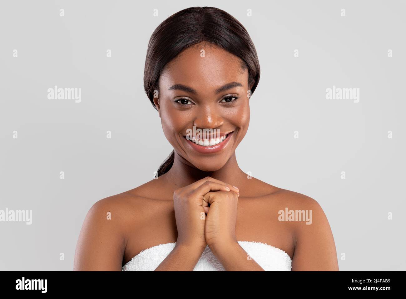 Fröhliche hübsche tausendjährige afroamerikanische Frau mit perfekter Haut in Handtuch isoliert auf grauem Hintergrund, Studio Stockfoto