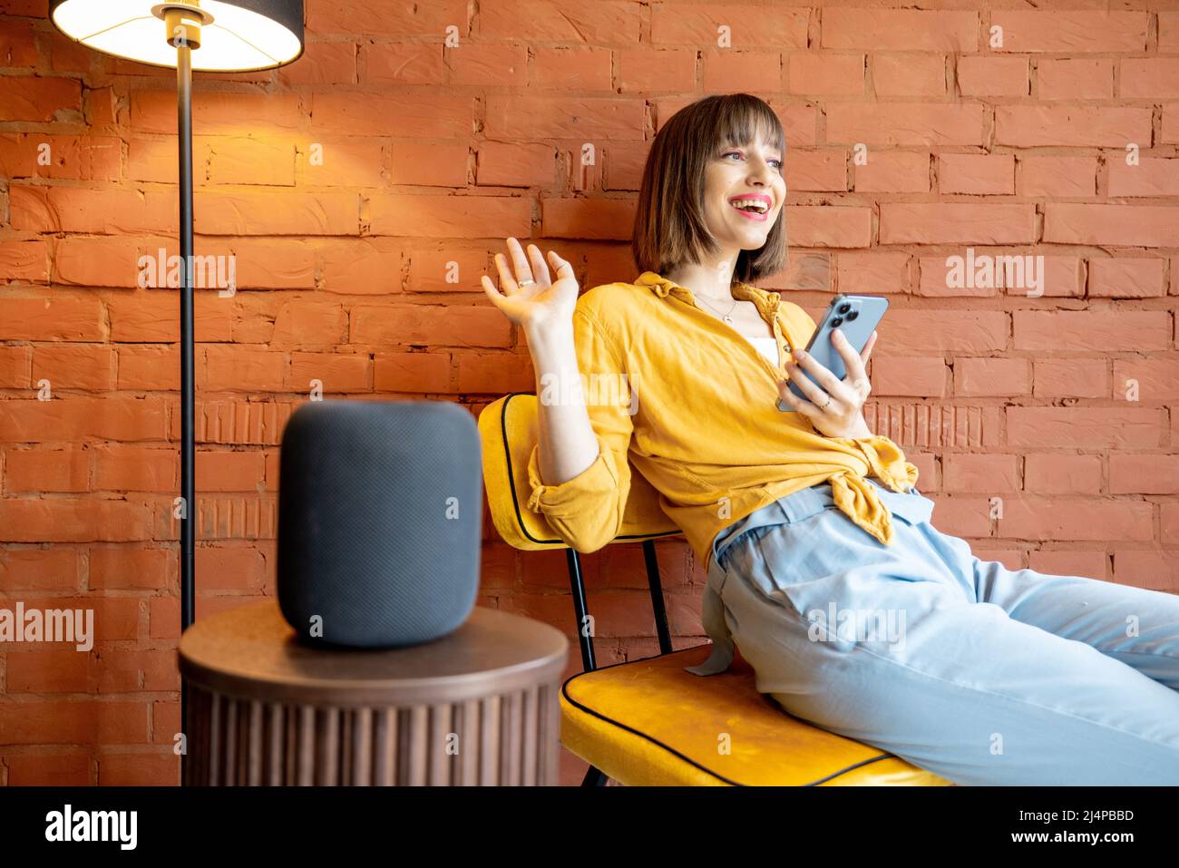 Frau mit Smart-Lautsprecher und Telefon zu Hause Stockfoto