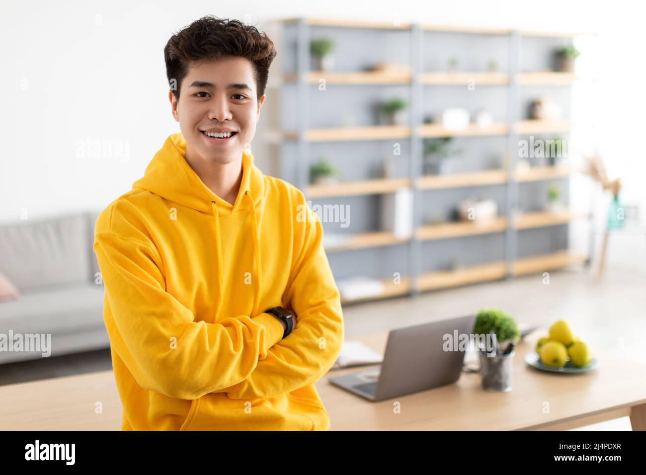 Bedingt lächelnder asiatischer Mann, der mit gefalteten Armen posiert Stockfoto