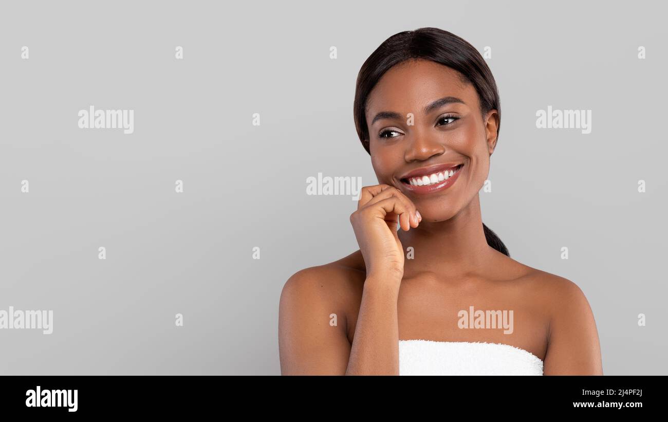 Lächelnde hübsche junge afroamerikanische Frau mit glänzendem Haar im Handtuch und Blick auf den freien Raum Stockfoto