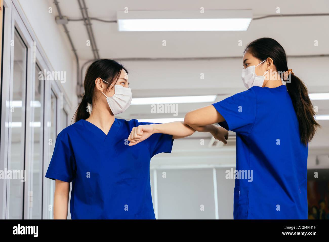 Junge weibliche Gesundheitshelferinnen, die eine OP-Maske tragen und die Hände mit Ellenbogenstoß schütteln, während sie während des Ausbruchs der Corona-Virus-Pandemie die soziale Distanz aufrechterhalten Stockfoto