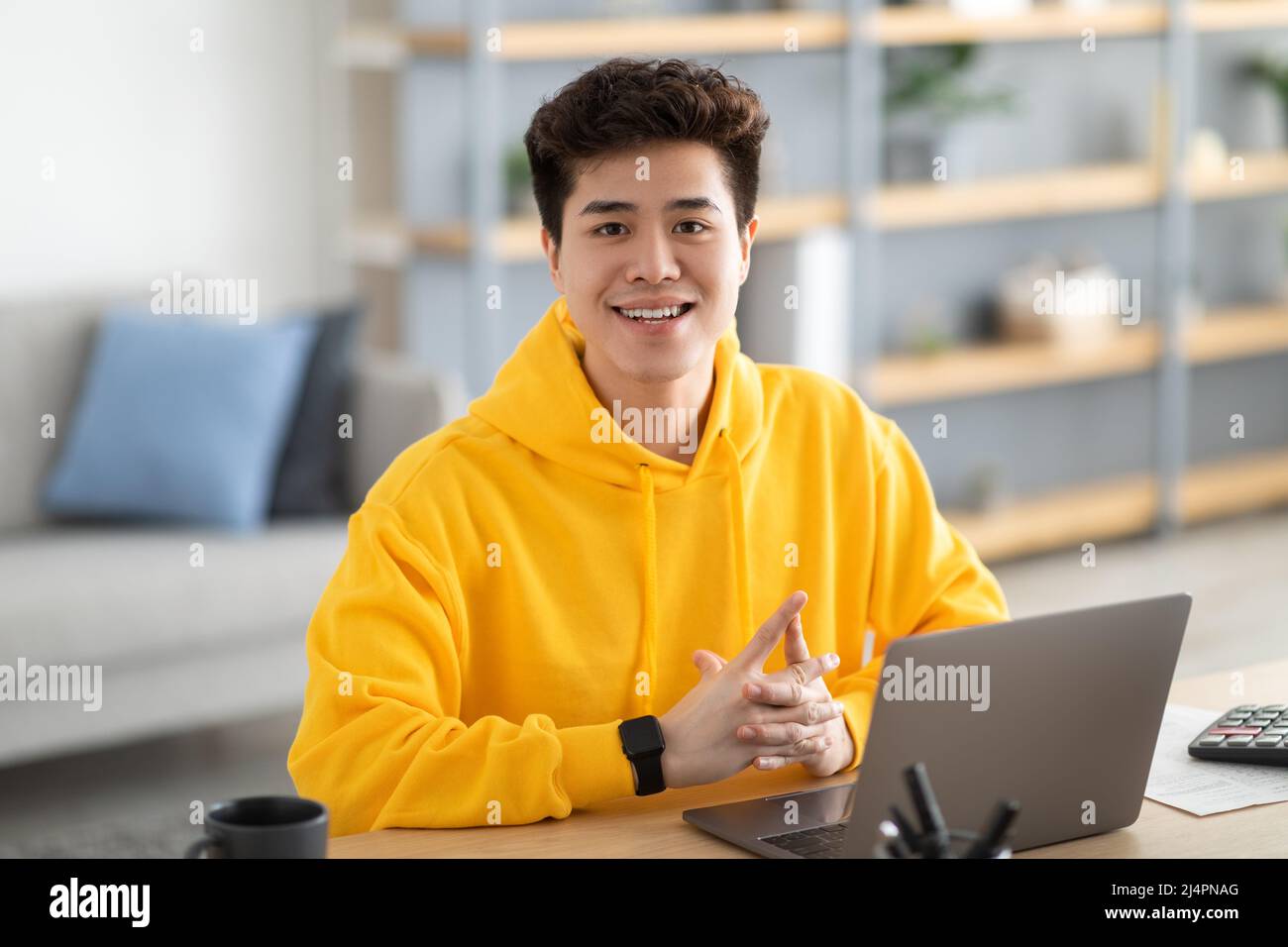 Am Schreibtisch sitzender, zustandig lächelnder asiatischer Mann, der posiert Stockfoto