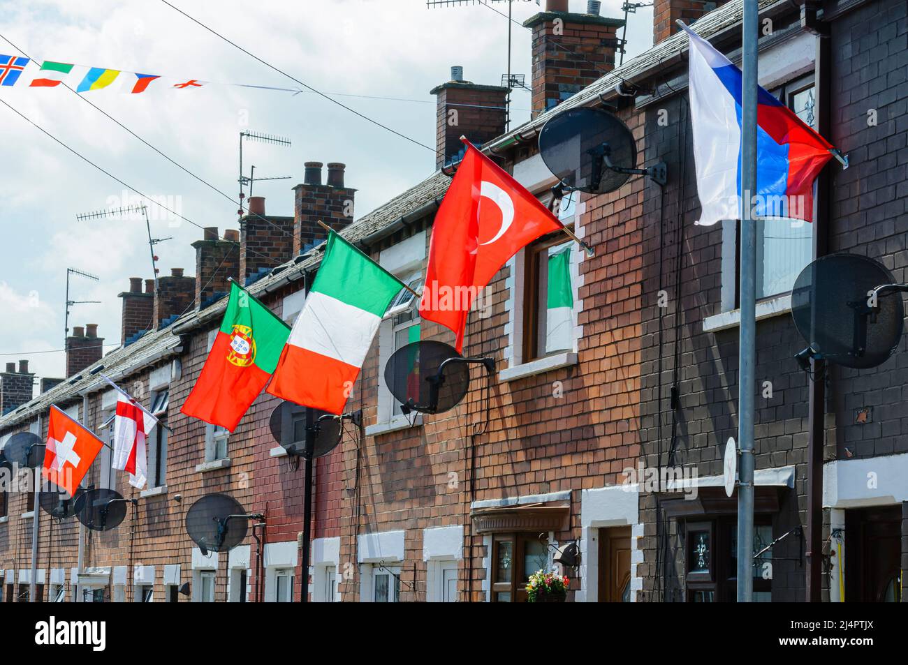 BELFAST, NORDIRLAND. 04 JUN 2016: Häuser im Iris Drive in West Belfast sind mit den Flaggen aller 24 Länder geschmückt, die sich für die Euro 2016 qualifiziert haben. Die Bewohner organisierten ein Gewinnspiel, bei dem jedes Haus die Flagge ihres Landes führen musste. Es wird angenommen, dass zum ersten Mal die Flaggen von England und Nordirland freiwillig in diesem unerschütterlichen republikanischen Gebiet von West-Belfast geflogen wurden. Stockfoto