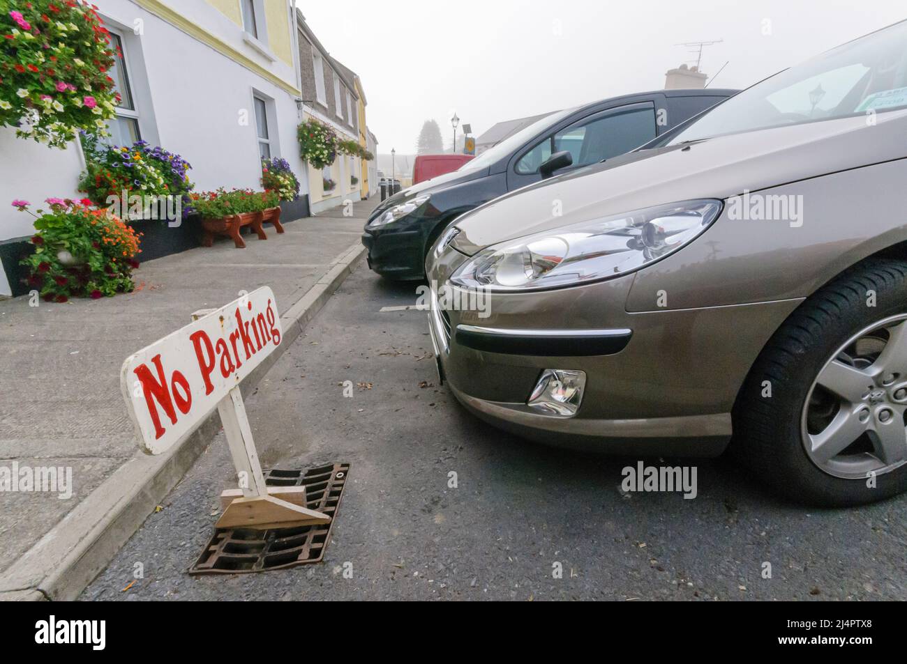 Schild, das die Leute auffordert, nicht zu parken, mit einem Auto, das auf dem Platz geparkt ist. Stockfoto