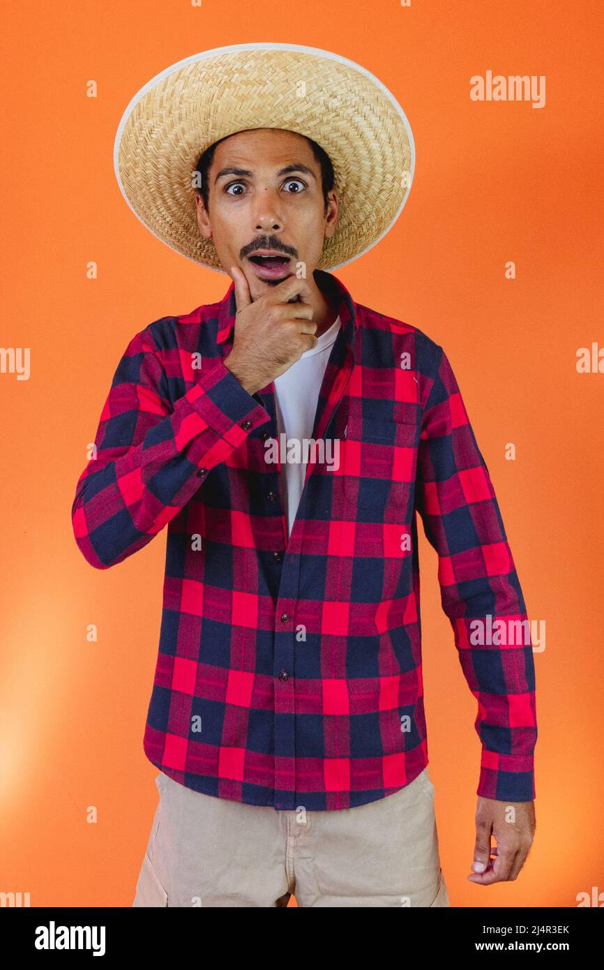 Schwarzer Mann mit Junina Party Outfit isoliert auf orangefarbenem Hintergrund. Junger Mann in traditioneller Kleidung für Festa Junina - brasilianisches Juni-Festival. Stockfoto