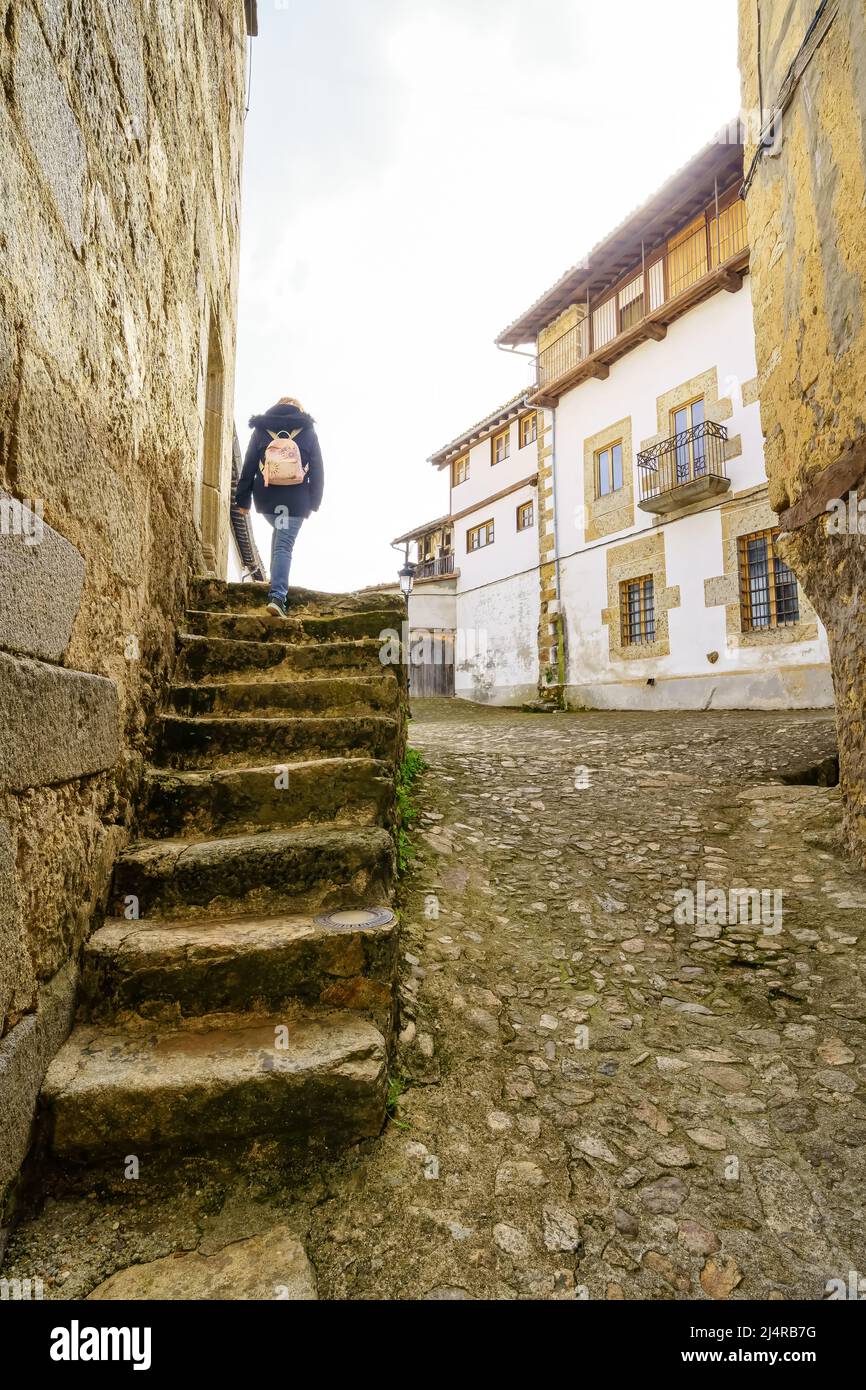 Frau klettert eine alte Steintreppe neben mittelalterlichen Häusern im Dorf Candelario, Salamanca. Stockfoto