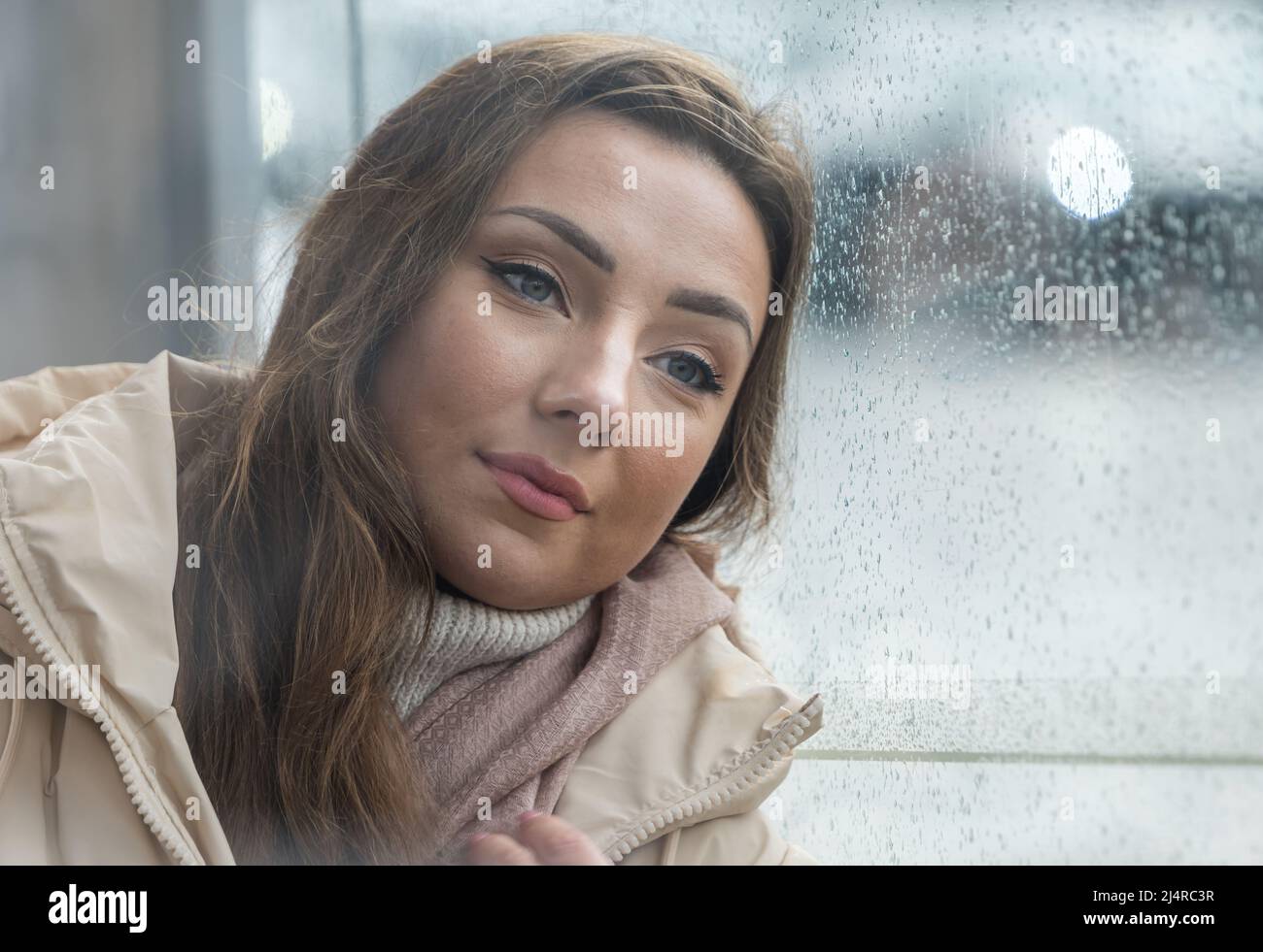 Eine hübsche junge Frau oder ein Model wartet wehmütig an einer Bushaltestelle an einem regnerischen Tag, Edinburgh, Schottland, Großbritannien Stockfoto