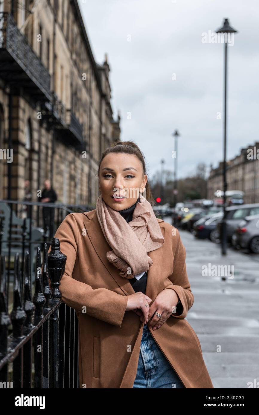 Eine hübsche junge Frau oder ein Model, das sich an Geländern in einer New Town Street, Edinburgh, Schottland, Großbritannien, stützt Stockfoto